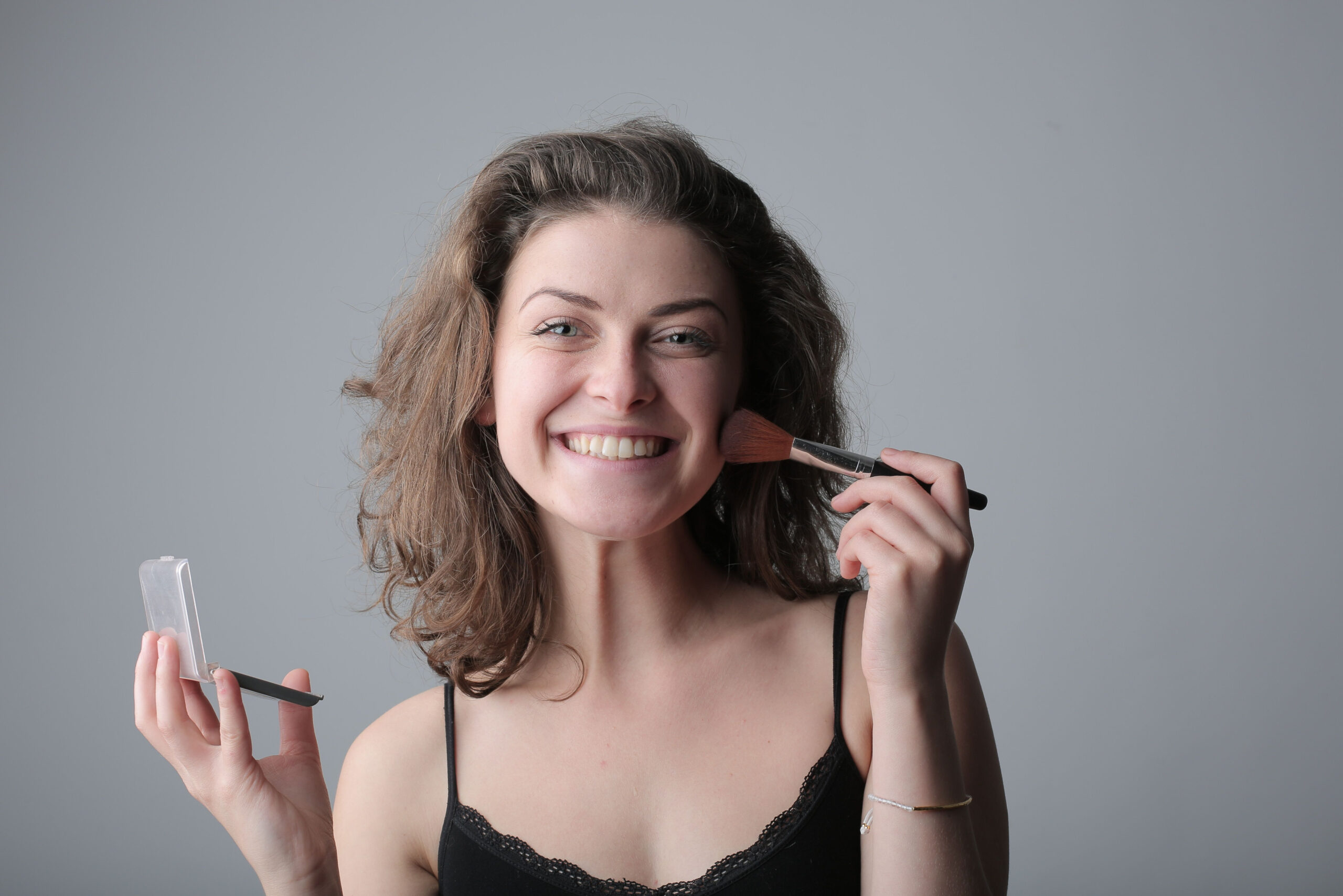 Smiling woman applying makeup, showing a brand that feels confident and connected